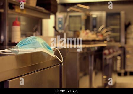 Chirurgische Maske in einer professionellen Küche, Konzept der Wiedereröffnung des Restaurants mit medizinischer Prävention Stockfoto