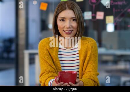 Porträt einer asiatischen Geschäftsfrau, die lächelt und den Kaffeebecher hält Im Tagungsraum Stockfoto