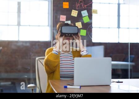 Porträt einer asiatischen Geschäftsfrau, die vor einem Laptop sitzt Virtual Reality-Headset Stockfoto