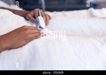 Mittelteil einer weiblichen Patientin mit gemischter Rasse, die im Krankenhausbett liegt Tragen des Pulsoximeters mit der Fingerspitze Stockfoto