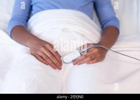 Mittelteil einer weiblichen Patientin mit gemischter Rasse, die im Krankenhausbett liegt Tragen des Pulsoximeters mit der Fingerspitze Stockfoto