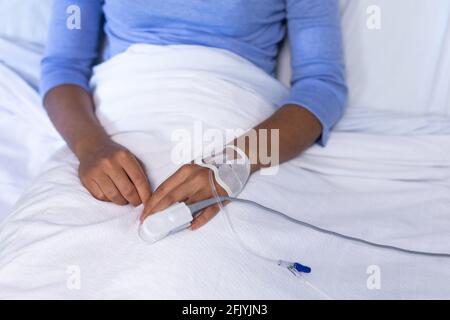 Mittelteil einer weiblichen Patientin mit gemischter Rasse im Krankenhausbett Pulsoximeter mit Fingerspitze und infusionsschlauch Stockfoto