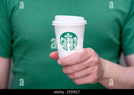 BERLIN - APR 25: а Mann in grünem T-Shirt mit weißem Papierbecher mit Starbucks-Logo im Starbucks-Restaurant in Berlin, April 25. 202 in deutscher Sprache Stockfoto