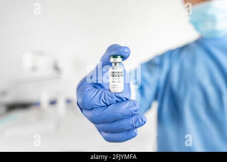 Nahaufnahme eines leitenden Arztes, einer Krankenschwester oder eines Pflegepersonals mit selektivem Fokus in einem persönlichen Schutzkit, in dem eine Ampulle mit Impfstoff zur Behandlung der aga gezeigt wird Stockfoto