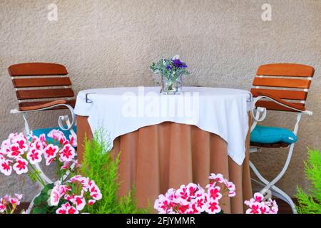 Tisch mit Tischdecke für Paare auf der Sommerterrasse des Restaurants. Wand aus altem strukturiertem Stein im Hintergrund. Stockfoto