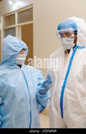 Vertikale Aufnahme von Medizinern in Schutzkleidung, Handschuhen und Masken, die etwas diskutieren Stockfoto
