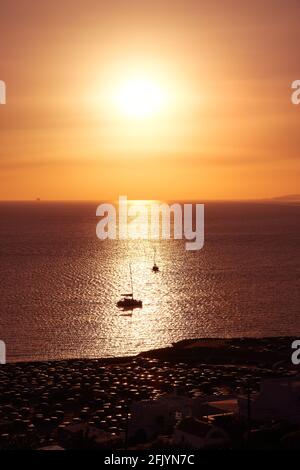 Herrliche Sonnenuntergangslandschaft. Niedrige Sonne am trüben Himmel und Sonneneinstrahlung auf dem ruhigen Meer. Kleine Segelboote im Sonnenstreifen, dunkle Küste. Romantisches Segeln. Stockfoto