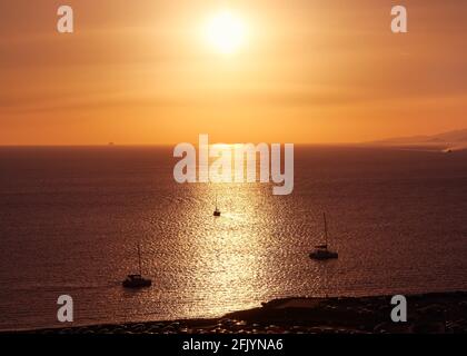 Herrliche Sonnenuntergangslandschaft. Niedrige Sonne am trüben Himmel, Sonnenblendung auf dem Meer. Kleine Segelboote, Sonnenstreifen, dunkle Küste. Sommerferien, romantisches Segeln. Stockfoto