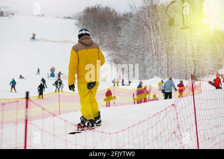 Snowboarder in gelb Skianzug erhebt sich auf heben Sie Berghang. Ski Sport im Winter. Urlaub in den Bergen im Skigebiet. Stockfoto