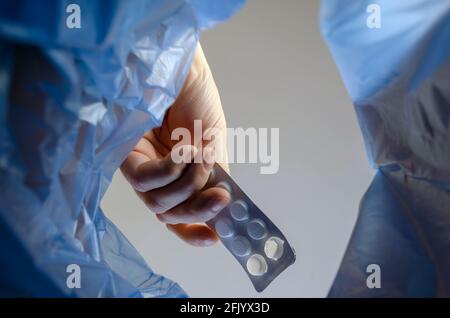 Die Hand wirft den Teller mit Pillen in den Müll. Ein Mann hält die unbrauchbaren abgelaufenen Medikamente über einem Abfalleimer in der Halle. Ansicht von unten. Stockfoto