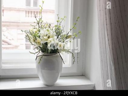 Osterfrühling Stillleben. Blumenstrauß auf der Fensterbank. Weiße und gelbe Tulpen, Narzissen und grüne Birken- und Heidelbeerzweige Stockfoto