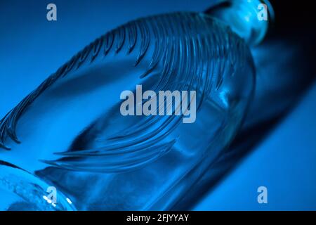 Abstrakte Glasflasche Hintergrund. Textur aus gewelltem Glas, beleuchtet mit mehrfarbigem Licht. Rosa und blaue Flecken. Nahaufnahme. Fackeln auf Glas Stockfoto