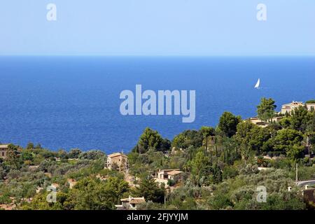 Eine breite Aufnahme von blauem Himmel und Meer mit dem Dorf Deià im Vordergrund; Mallorca, Balearen, Spanien. Nachmittag im September. Stockfoto