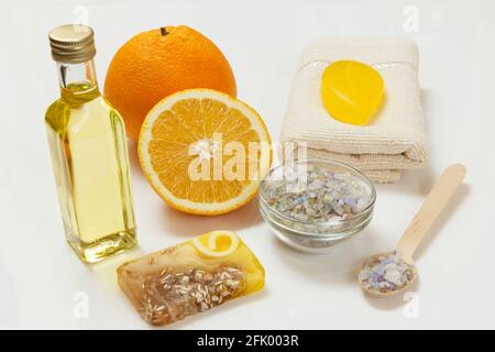 Schneiden Sie Orange mit einem ganzen Stück, einem Frottee-Handtuch, einer Flasche mit Aromatherapieöl, Seife, einer Schüssel und einem Holzlöffel mit Meersalz auf weißem Grund. Spa Stockfoto