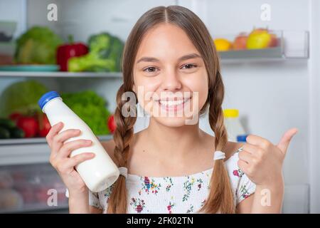 Schöne junge Teenager-Mädchen hält Flasche Milch und Getränke Während Sie in der Nähe des offenen Kühlschranks in der Küche zu Hause stehen Stockfoto