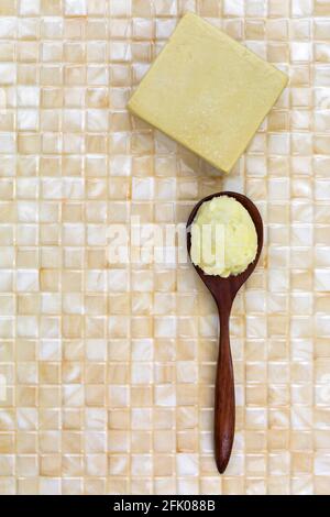 Sheabutter in Holzlöffel, hausgemachte Olivenölseife auf gelbem Fliesenhintergrund mit Copyspace Stockfoto