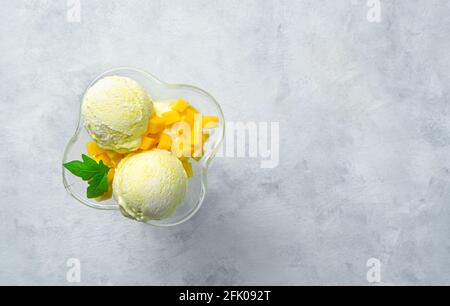 Zwei Kugeln Mangoeis und Scheiben frischer Mango auf grauem Hintergrund mit Platz zum Kopieren. Draufsicht. Sommerdessert. Stockfoto