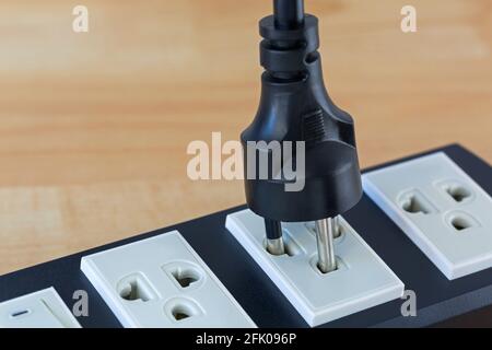 Thai 2 runder Netzstecker mit Erdstecker zum Einstecken in kompatibles Verlängerungskabel, mit verwaschenem Holzhintergrund für Copyspace Stockfoto