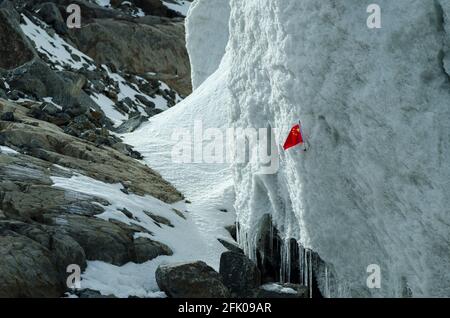 Am Rand des Gletschers wurde von chinesischen Touristen eine chinesische Flagge am Xinjiang Tianshan No 1 Gletscher hinterlassen, wo Eis und Schnee über viele Jahre auf die felsigen Hänge der Tianshan Berge im Osten von Xinjiang, China, PRC, verdichtet wurden. © Time-Snaps Stockfoto