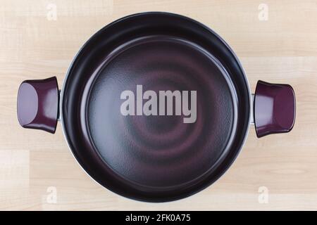 Großer, beschichteter Stewpot, Kochtopf in dunkelviolettem, schwarzem und schwarzem Farbton. Kochgeschirr mit Induktionstechnologie auf Holzhintergrund, Draufsicht Stockfoto