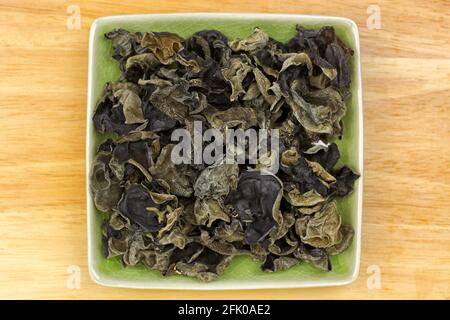 Getrockneter chinesischer essbarer schwarzer Pilz, genannt Judenohr Pilz in grüner Schale, Draufsicht auf Holzhintergrund Stockfoto