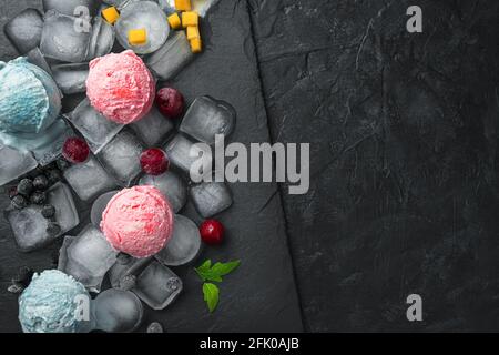 Kugeln aus Beereneis auf Eisstücken auf einem schwarzen Tisch. Draufsicht, Nahaufnahme. Sommerdesserts. Stockfoto