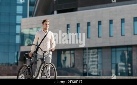 Persönlicher Öko-Transport, Sport, aktiver Lebensstil, Fahrradfahrer und Straße ins Büro. Lächelnder, tausendjähriger, hübscher Kaukasianer in formeller Kleidung geht mit Stockfoto