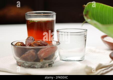 Getrocknete Datteln, ramadan getrocknete Datteln in einer Glasschale mit einem Glas reinem Trinkwasser und Zitronentee auf einer weißen Textur platziert, selektiver Fokus. Stockfoto