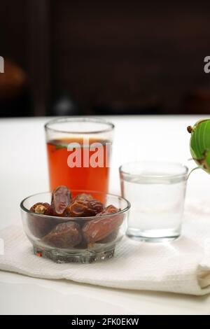 Getrocknete Datteln, ramadan getrocknete Datteln in einer Glasschale mit einem Glas reinem Trinkwasser und Zitronentee auf einer weißen Textur platziert, selektiver Fokus. Stockfoto