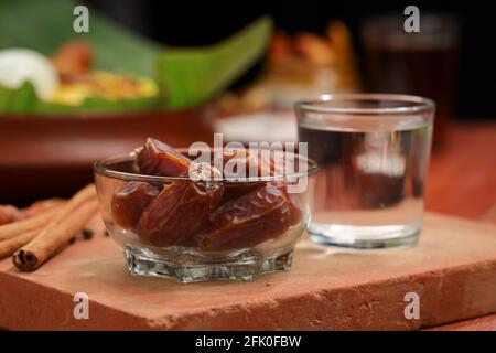Getrocknete Datteln, ramadan getrocknete Datteln in eine Glasschale mit gestellt Ein Glas reines Trinkwasser auf ein Holz gelegt Textur mit Biryani und Beilage in Th Stockfoto