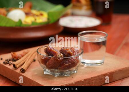 Getrocknete Datteln, ramadan getrocknete Datteln in eine Glasschale mit gestellt Ein Glas reines Trinkwasser auf ein Holz gelegt Textur mit Biryani und Beilage in Th Stockfoto