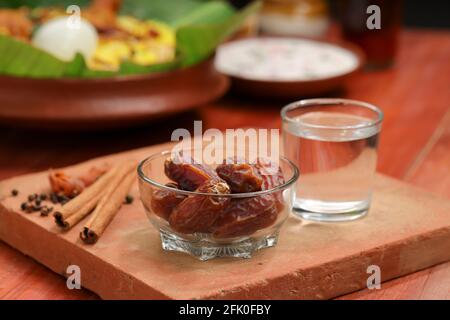 Getrocknete Datteln, ramadan getrocknete Datteln in eine Glasschale mit gestellt Ein Glas reines Trinkwasser auf ein Holz gelegt Textur mit Biryani und Beilage in Th Stockfoto