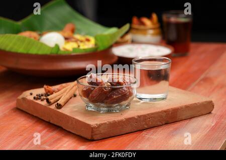 Getrocknete Datteln, ramadan getrocknete Datteln in eine Glasschale mit gestellt Ein Glas reines Trinkwasser auf ein Holz gelegt Textur mit Biryani und Beilage in Th Stockfoto