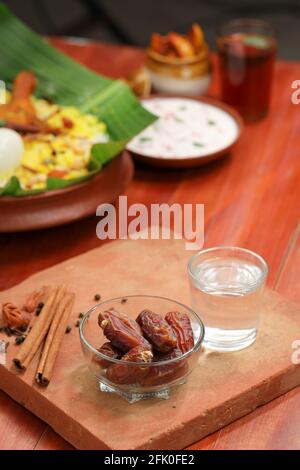 Getrocknete Datteln, ramadan getrocknete Datteln in eine Glasschale mit gestellt Ein Glas reines Trinkwasser auf ein Holz gelegt Textur mit Biryani und Beilage in Th Stockfoto