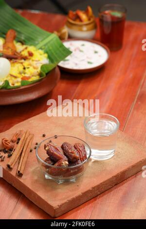 Getrocknete Datteln, ramadan getrocknete Datteln in eine Glasschale mit gestellt Ein Glas reines Trinkwasser auf ein Holz gelegt Textur mit Biryani und Beilage in Th Stockfoto