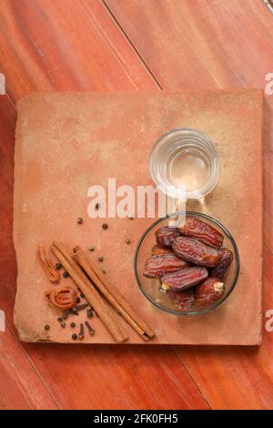 Getrocknete Datteln, ramadan getrocknete Datteln in einer Glasschale mit einem Glas reinem Trinkwasser auf einer Holzstruktur platziert, selektiver Fokus. Stockfoto