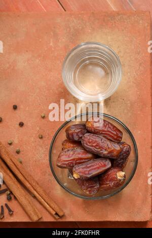 Getrocknete Datteln, ramadan getrocknete Datteln in einer Glasschale mit einem Glas reinem Trinkwasser auf einer Holzstruktur platziert, selektiver Fokus. Stockfoto