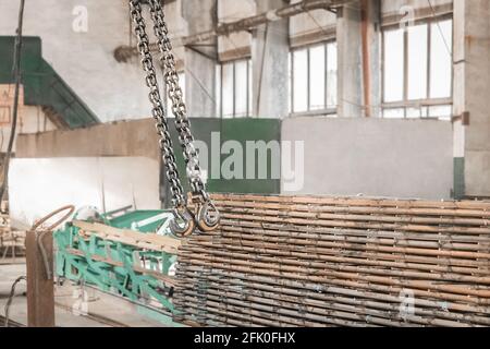 Hebemechanismus eines Brückenkrans mit Haken und Kette neben der Verstärkung der Eisenkonstruktionen in der Werkstatt eines Industrieunternehmens. Stockfoto