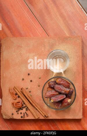 Getrocknete Datteln, ramadan getrocknete Datteln in einer Glasschale mit einem Glas reinem Trinkwasser auf einer Holzstruktur platziert, selektiver Fokus. Stockfoto
