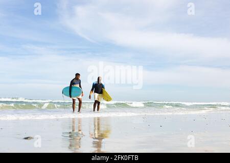 afroamerikanischer Vater und Sohn mit Surfbrettern, die in Richtung der gehen Strand Stockfoto