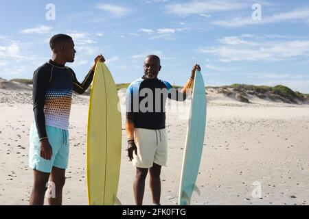 afroamerikanischer Vater und Sohn mit Surfbrettern, die an der stehen Strand Stockfoto