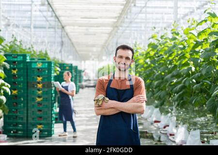 Fröhlicher Bauer lächelt der Kamera zu, während ein afroamerikanischer Kollege arbeitet Auf unscharfem Hintergrund Stockfoto