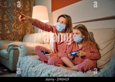 Frau und junges Mädchen tragen Schlafanzug und medizinische Schutzmaske Stockfoto