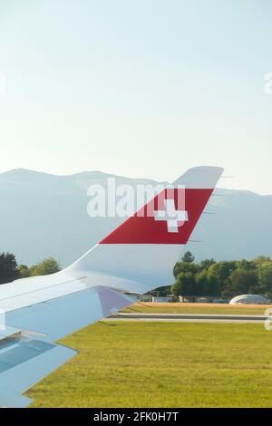 Blick auf den Flugzeugflügel mit der Schweizer Logo-Flagge / dem Flugzeugflügel einer Bombardier C-Serie und die Berglandschaft rund um den Flughafen Genf/Genf, Schweiz. (101) Stockfoto