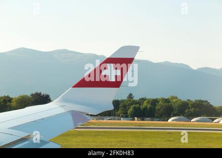 Blick auf den Flugzeugflügel mit der Schweizer Logo-Flagge / dem Flugzeugflügel einer Bombardier C-Serie und die Berglandschaft rund um den Flughafen Genf/Genf, Schweiz. (101) Stockfoto