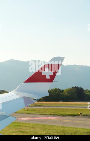 Blick auf den Flugzeugflügel mit der Schweizer Logo-Flagge / dem Flugzeugflügel einer Bombardier C-Serie und die Berglandschaft rund um den Flughafen Genf/Genf, Schweiz. (101) Stockfoto