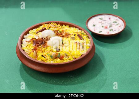 Ei Biryani , kerala Stil biriyani aus Jeera Reis und Gewürze in einem irdenen Geschirr mit Raitha als Beilage auf grünem strukturierten Hintergrund angeordnet gemacht Stockfoto