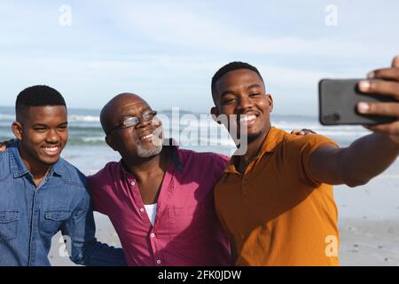 afroamerikanischer Vater und seine beiden Söhne beim Selfie Vom Smartphone am Strand Stockfoto