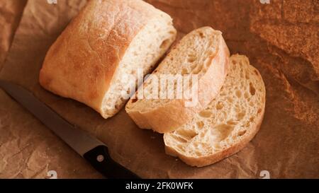 Der Koch schneidet die Ciabatta mit einem Messer in Scheiben. Ciabatta-Scheiben auf Bastelpapier. Frisches, köstliches Gebäck. Frisches, hausgemachtes Brot. Gesunde Ernährung Stockfoto