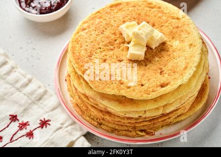 Crepes oder dünne Pfannkuchen stapeln mit Butter und Himbeermarmelade auf einer schönen Keramikplatte auf einem alten grauen Betonhintergrund. Draufsicht, Kopierbereich. Homem Stockfoto